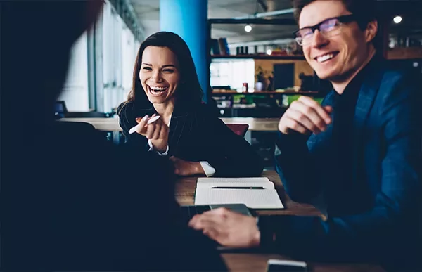 Group of people smiling and having a discussion in a modern office setting.
