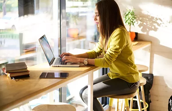 Person working on a laptop at a bright, cozy cafe.