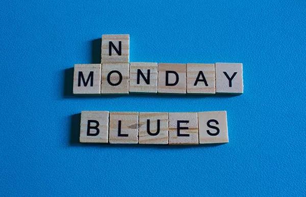 Scrabble tiles spell 'Monday Blues' on a blue surface.