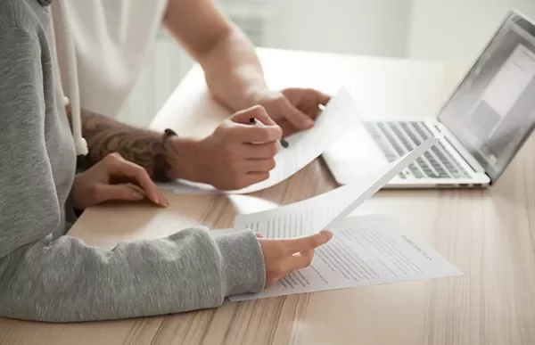 Two people reviewing documents at a table with a laptop.