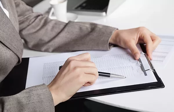 Person in suit reviewing documents with clipboard.