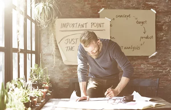 Person working at a desk with plants and notes on the wall.