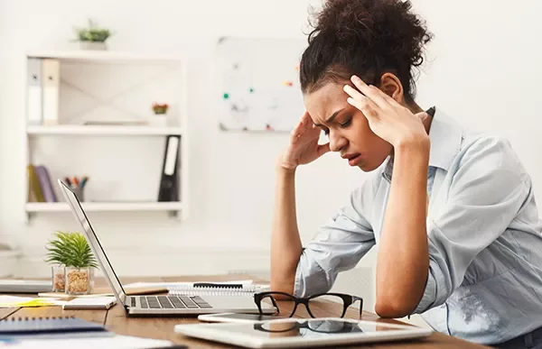 Person sitting at a desk, looking at a laptop with a thoughtful expression.