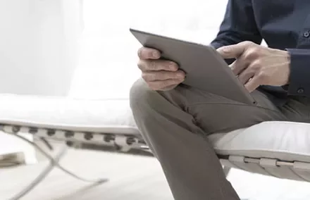Person sitting on a white sofa using a tablet.