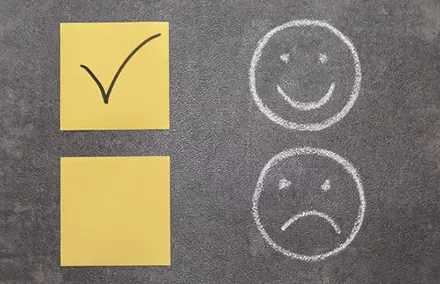 Yellow sticky notes with a check mark and boxes, chalk smiley and sad face on a blackboard.