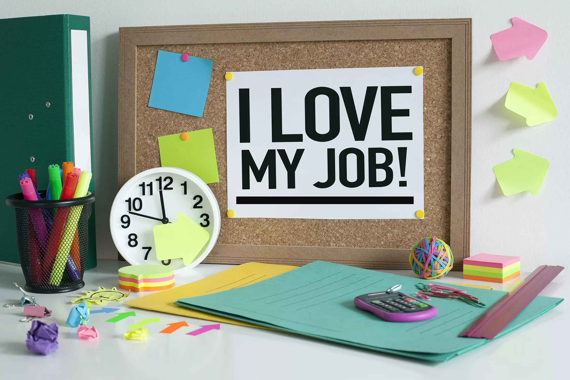 Desk scene with a bulletin board saying 'I love my job!' above office supplies.