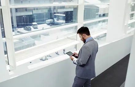 Person in a suit uses a tablet while standing near a large window.