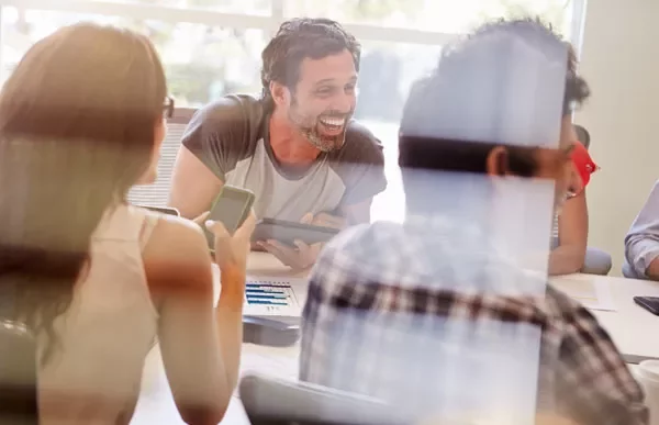 Group in a meeting, laughing and discussing something on a tablet.