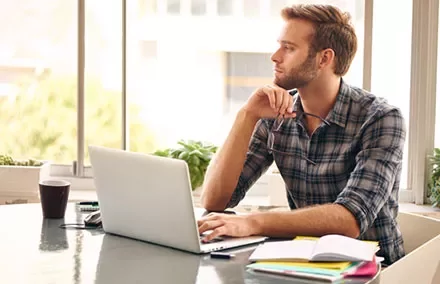 Person sitting at a desk with a laptop, looking out the window.