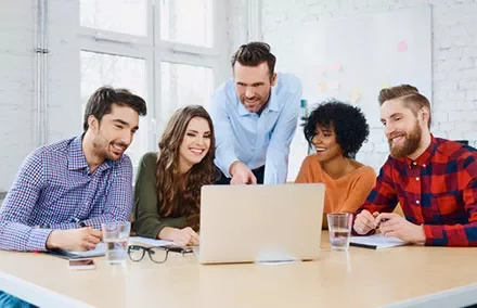 A group of people gathered around a laptop in a bright office.