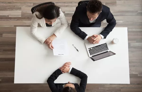 Top view of a job interview with three people at a table, one holding a resume.