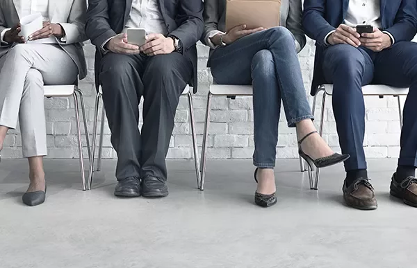 Four people seated in a row, each holding a device or document.