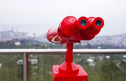 Red binoculars on a viewing platform overlook a cityscape.