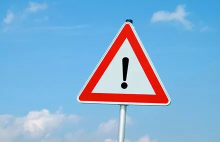 Triangular warning sign with exclamation mark against a blue sky.