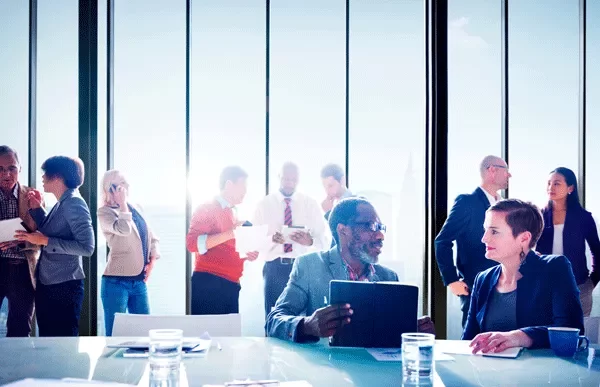 A group of professionals engaged in conversation and work in a bright office space.