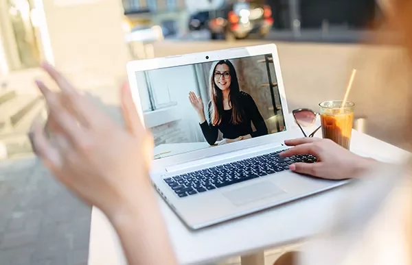 Person video calling on a laptop outdoors, waving at someone on the screen.