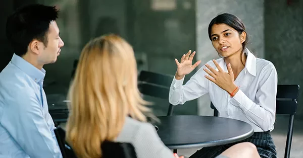 Person speaking passionately during a group discussion at a table.