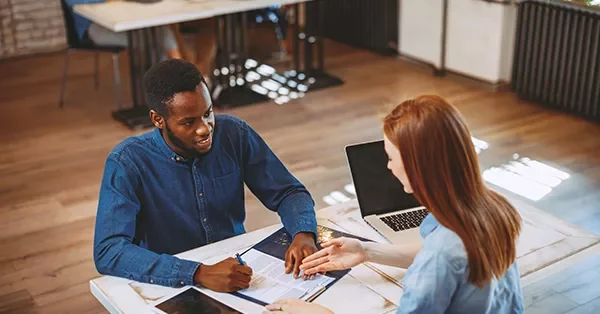 Two people discussing paperwork at a table with a laptop.