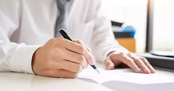 Person in formal attire writing with a pen on a desk.
