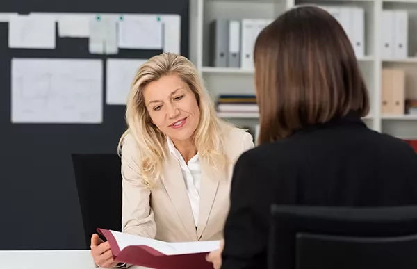 Two people sitting at a desk, discussing a document in an office setting.
