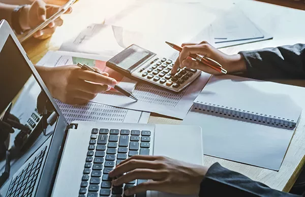 Hands using calculators and laptops on a desk with documents.