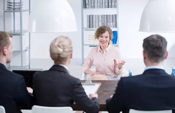 Person smiling during an interview, seated across a table from three people in an office setting.