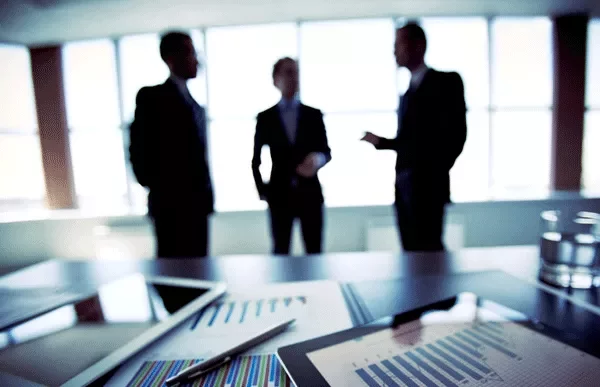 Business meeting with charts on table and three people discussing.