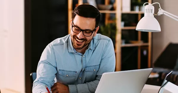 Person smiling while working on a laptop in a cozy office.